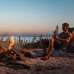 Happy young friends resting by the bonfire near tent.