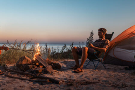 Happy young friends resting by the bonfire near tent.